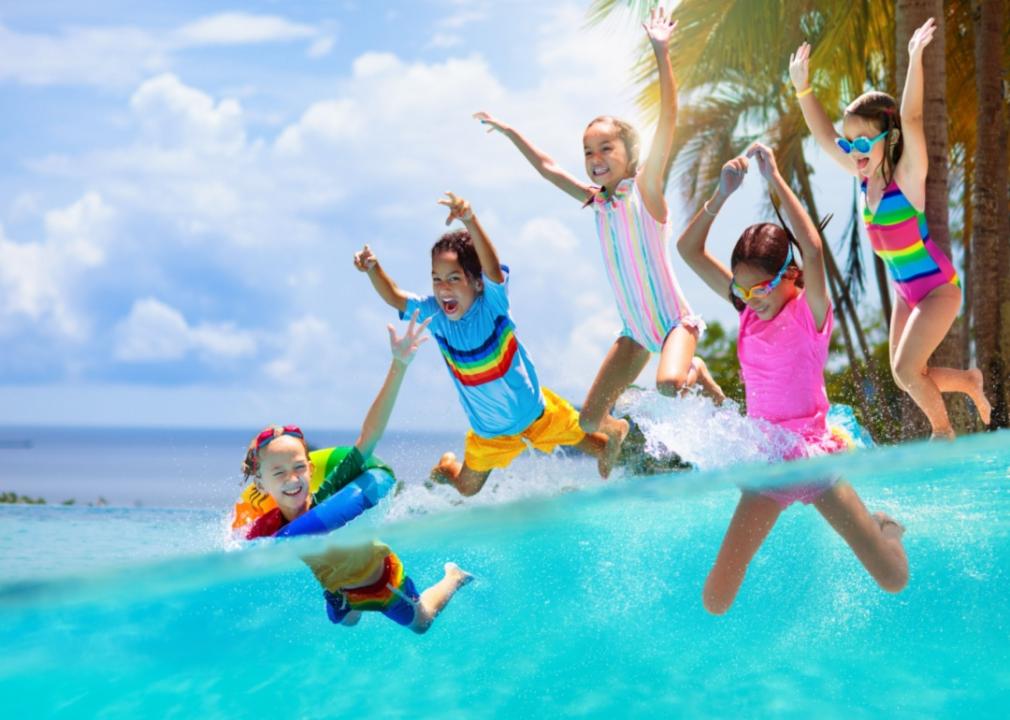 A group of kids in colorful swimwear jumping into a pool.