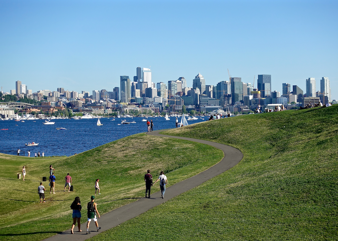 People walking in a park on the water with downtown Seattle in the background.