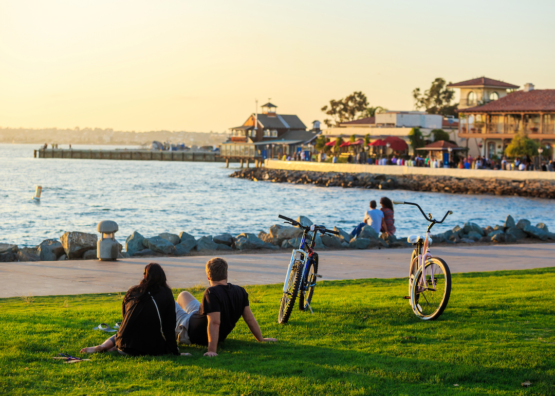 People sitting in the grass by the water with bicycles parked on the side.