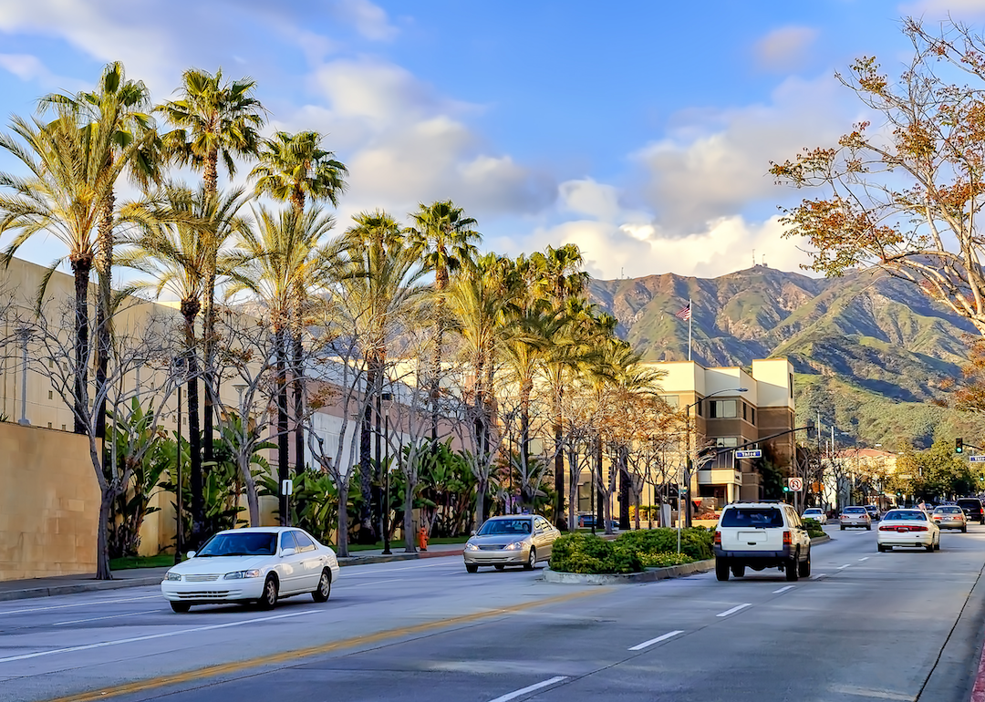 A street lined with palm trees and mountains in the background.