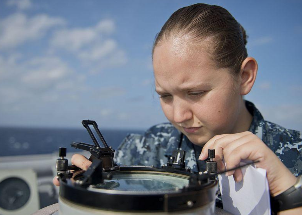 A soldier on a ship looking into an instrument.