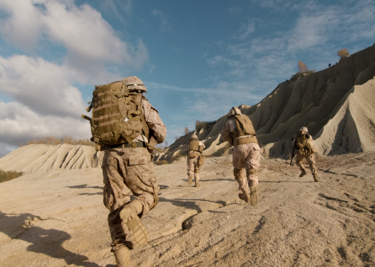 Soldiers in camo running in a desert landscape.