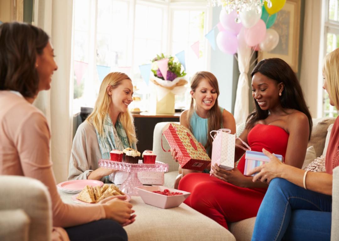 A group of women watching a mother-to-be open gifts.
