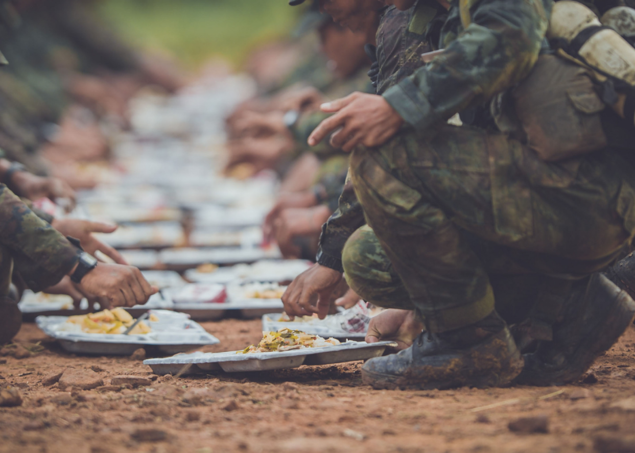 Soldiers leaning over to get plates of food on the ground.