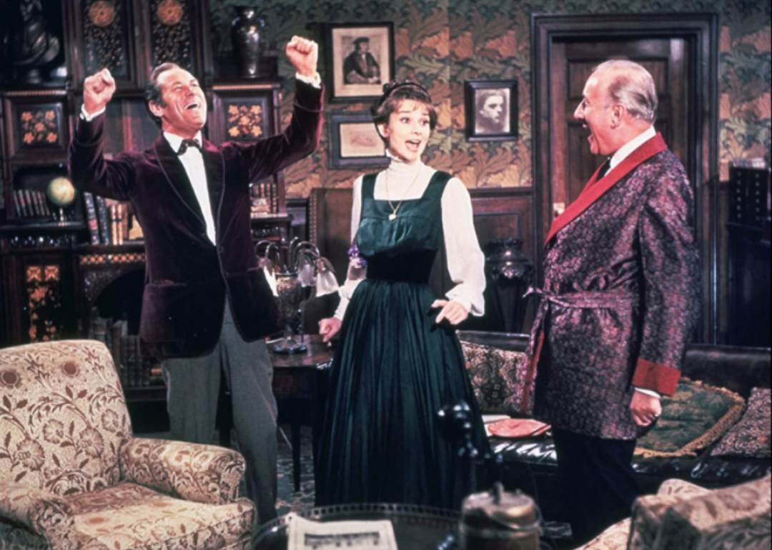 Audrey Hepburn and two men cheering in a lavish living room.