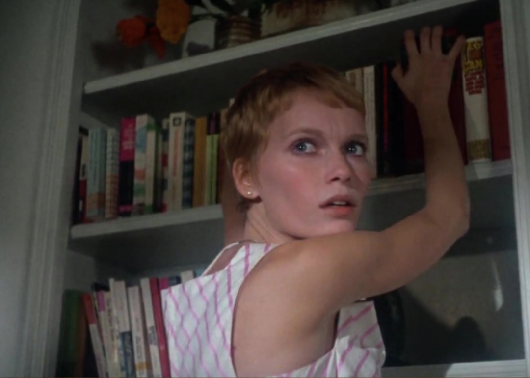 Mia Farrow looks back as she reaches up to a bookshelf.