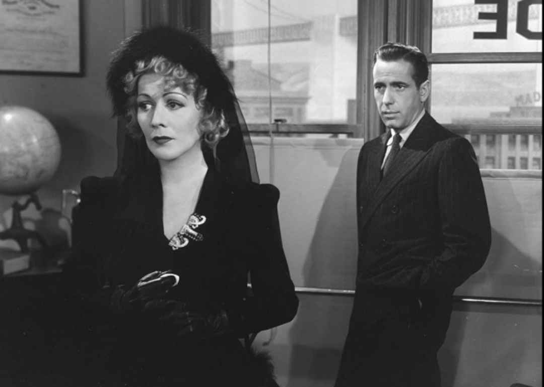 Humphrey Bogart and a woman in all black standing together.
