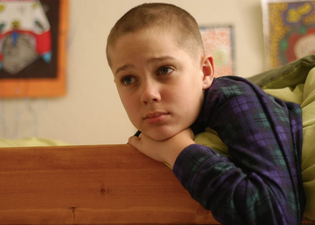 A young boy leaning over his bed.