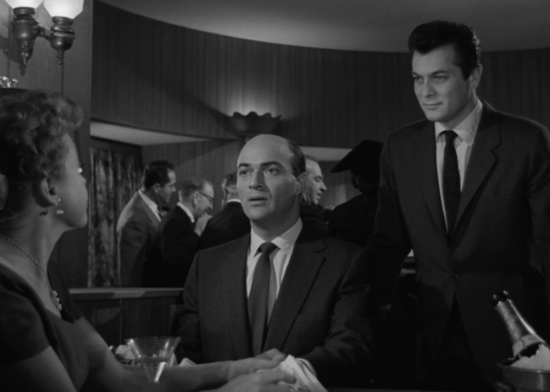 Two men in suits talking to a woman in a restaurant.