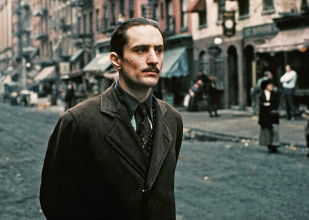 Robert De Niro with a mustache in a jacket and tie in the street.