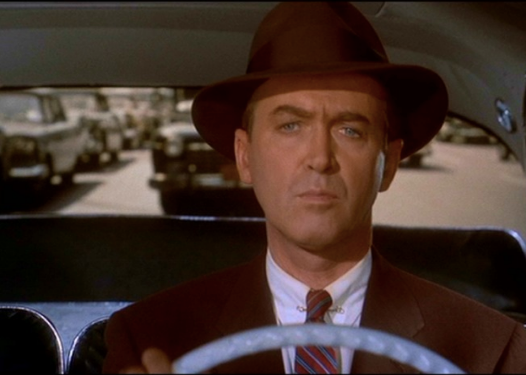 James Stewart, wearing a brown hat, driving a car.