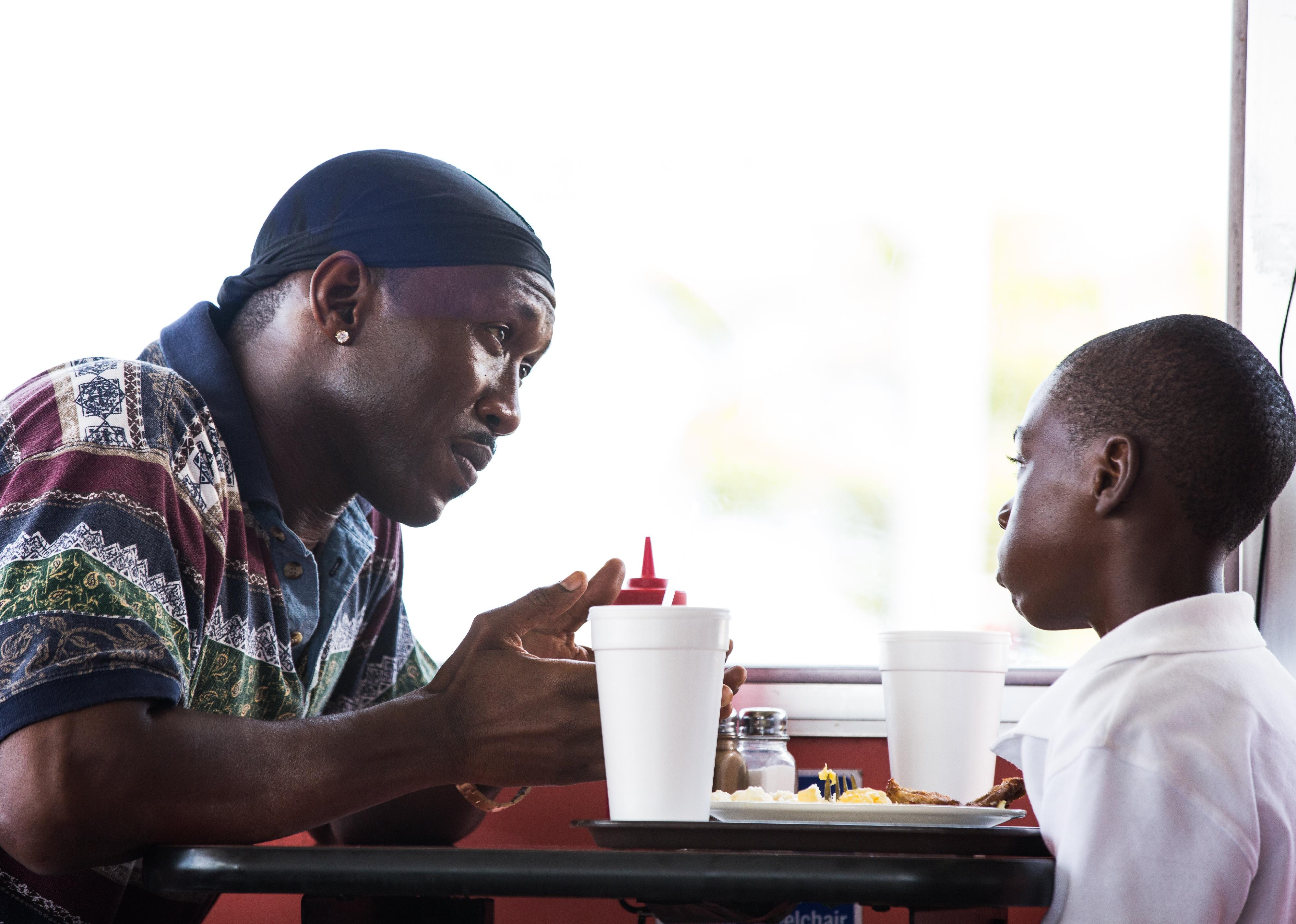 Mahershala Ali talking to a little boy eating at a diner.