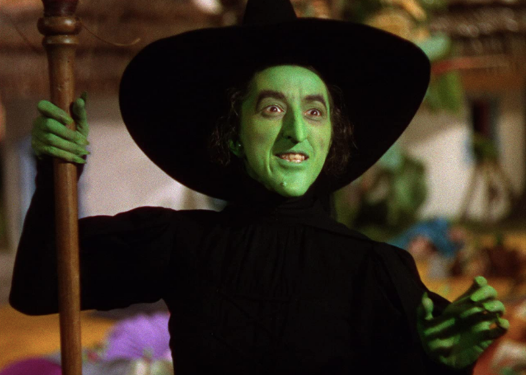 A witch in all black with a green face and hands.