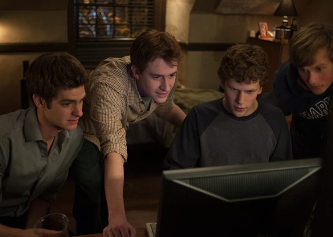 Joseph Mazzello, Jesse Eisenberg, Andrew Garfield, and Patrick Mapel looking at a computer screen.