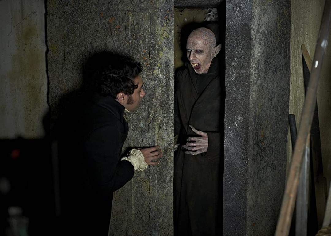 A human-like creature with sharp teeth and long fingers wearing a black long coat hisses at a man from inside a closet.