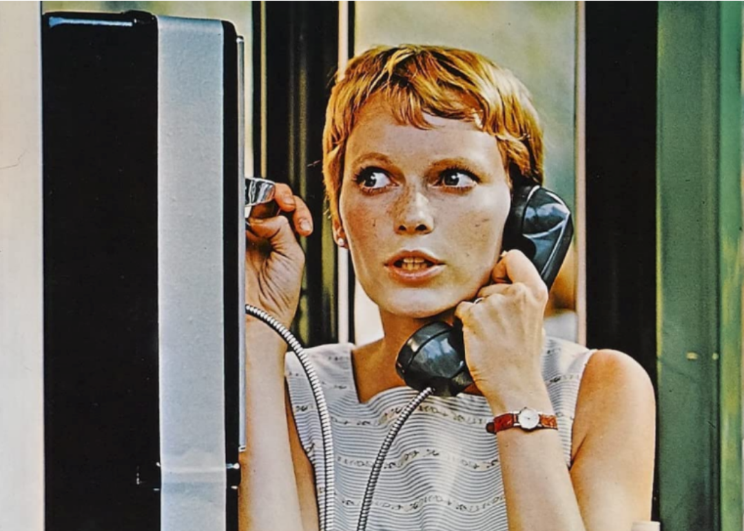 A short haired blonde woman talks on a pay phone.