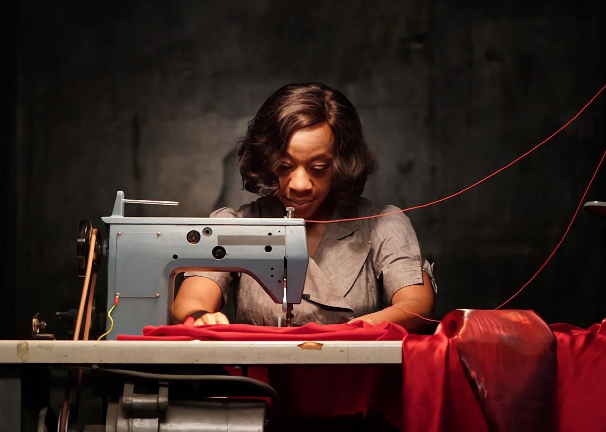 A middle aged woman sews a red dress on a vintage looking sewing machine.