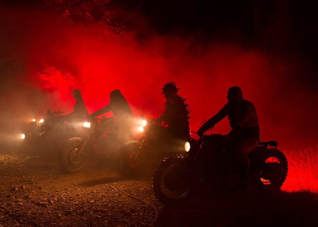 Four people ride motorcycles in the dark with a red light beaming behind them.