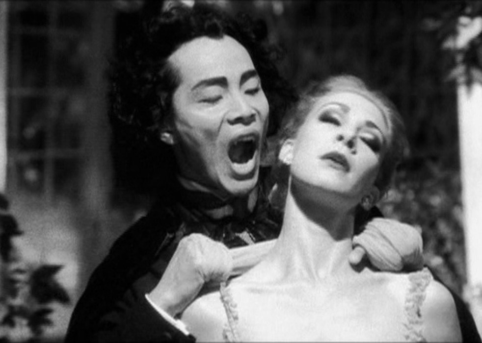 A man with vampire fangs poised to bite the neck of a woman.