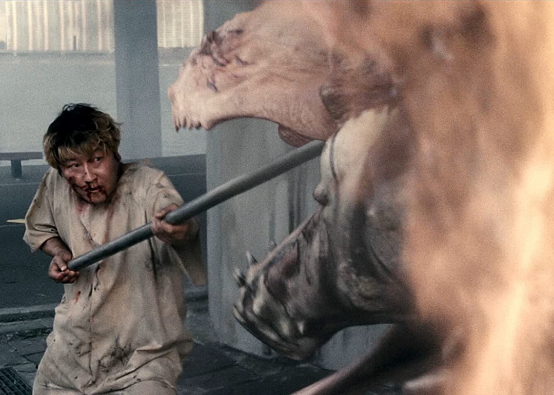 A bloody man shoves a long metal pole into the jaws of a giant creature.