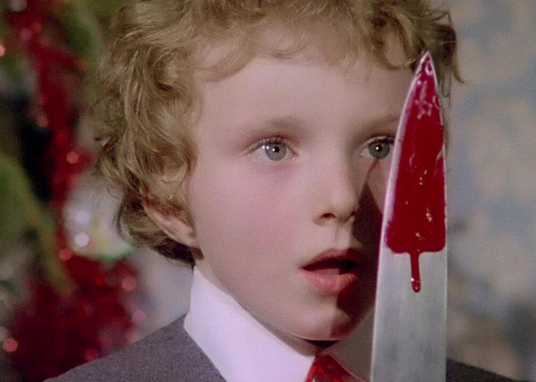 A little boy in a suit stares closely at a bloody knife.