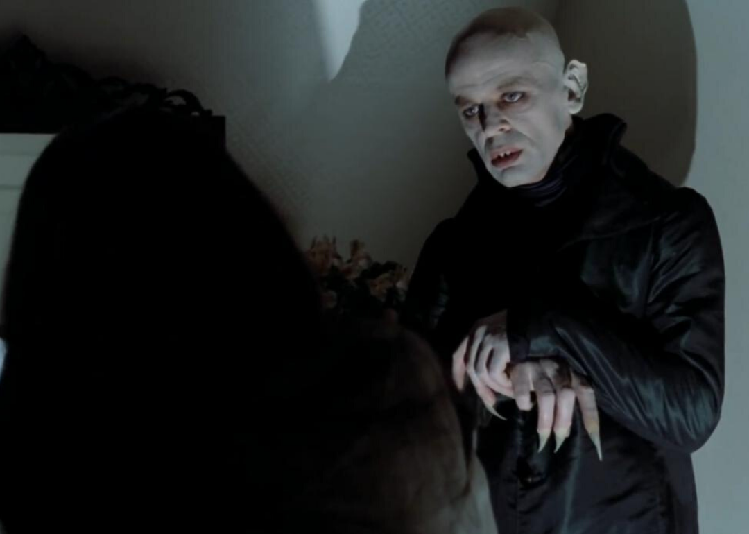 A pale bald man with long fingers and sharp teeth dressed in all black.