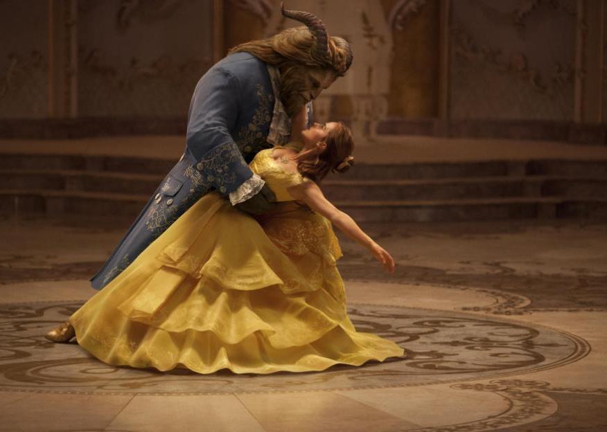 A woman in a yellow gown dancing with a beast in a blue suit.