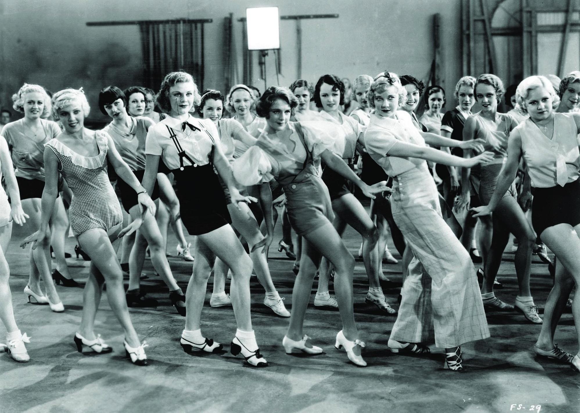 Ginger Rogers and a room full of girls practicing dancing.