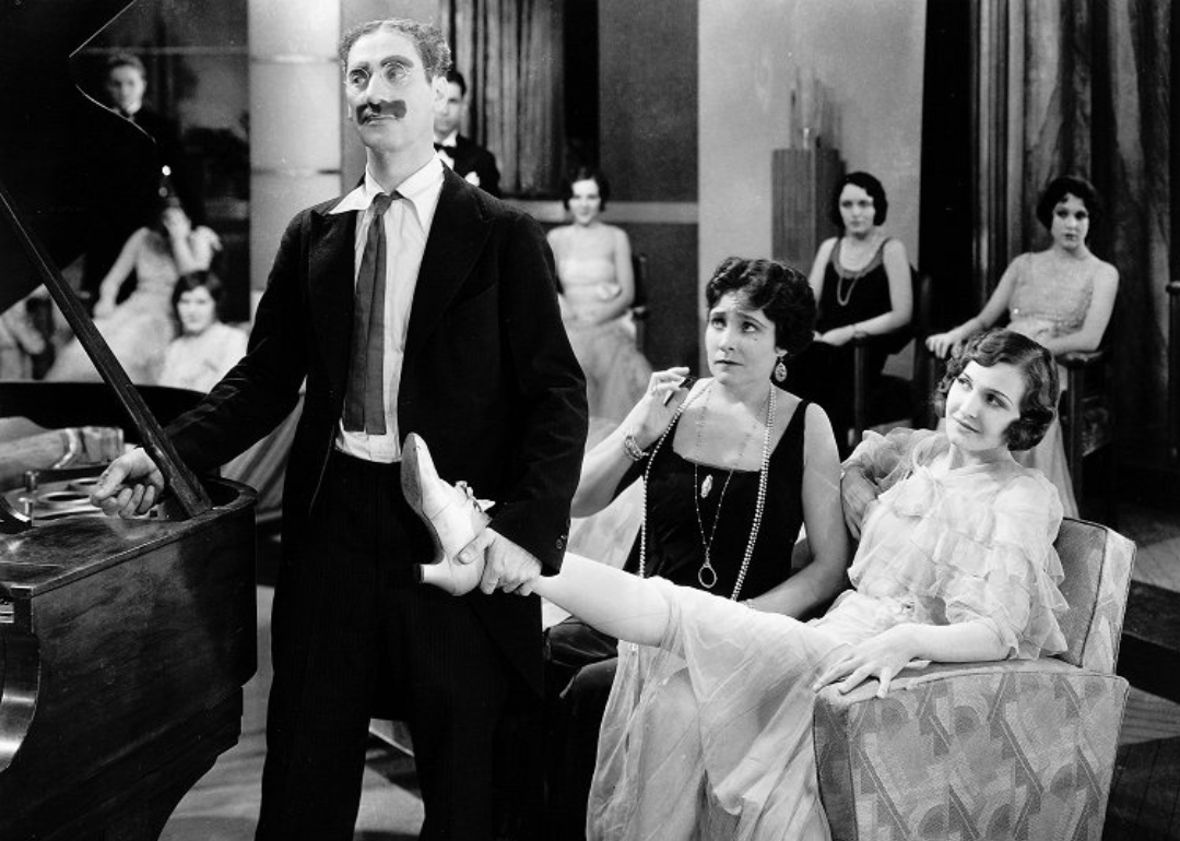 Groucho Marx next to a piano holding up a woman