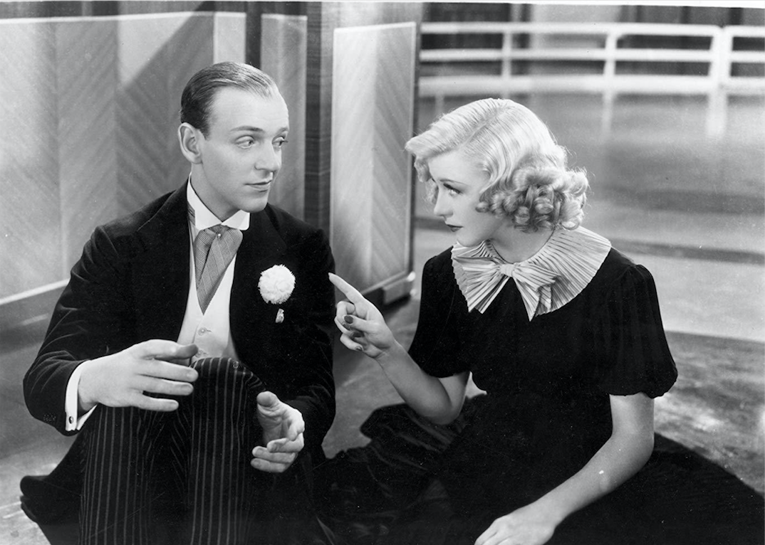 Fred Astaire and Ginger Rogers sitting on the floor together dressed up.