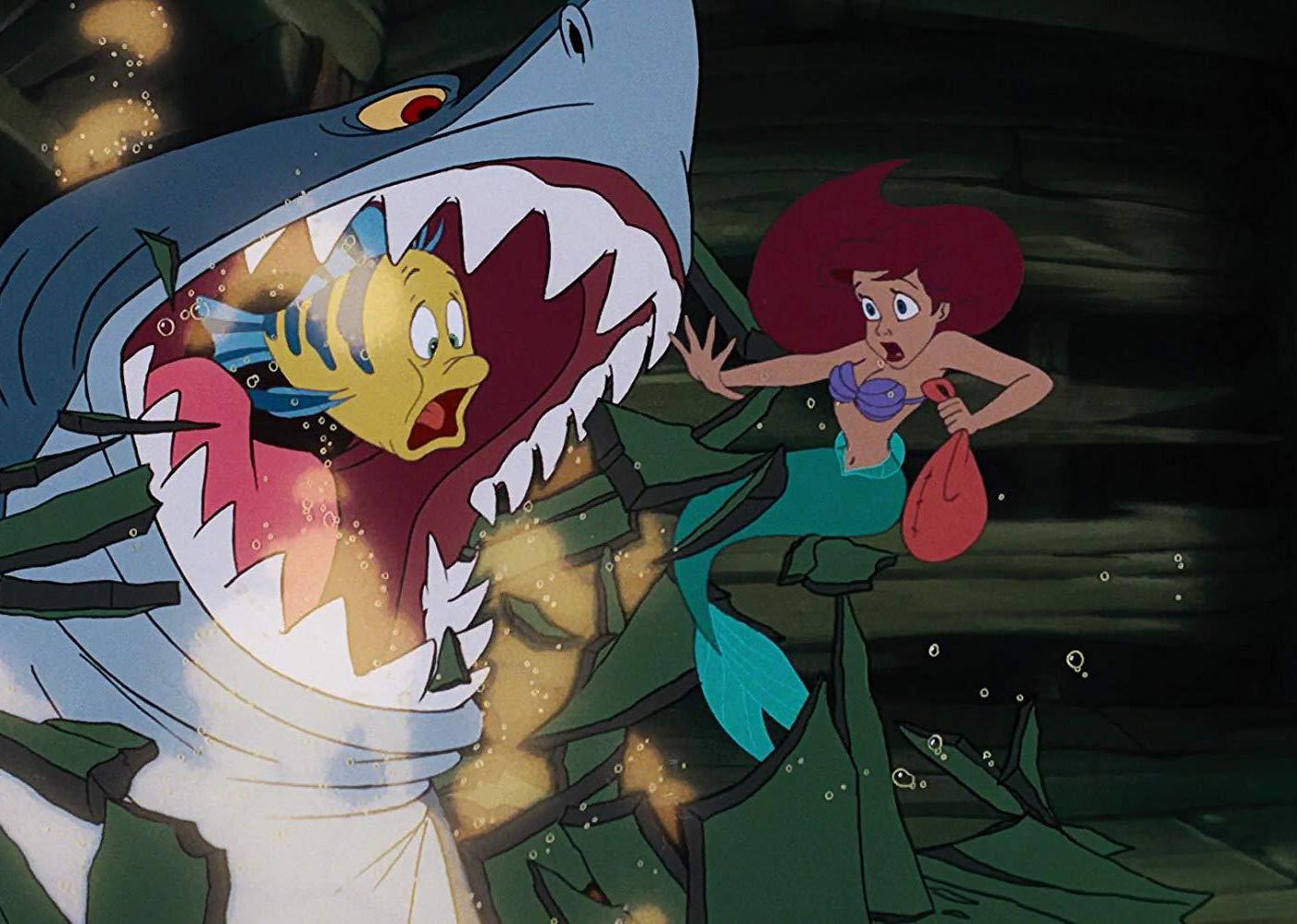 The Little Mermaid in shock looking at an open shark's mouth with a small fish inside.