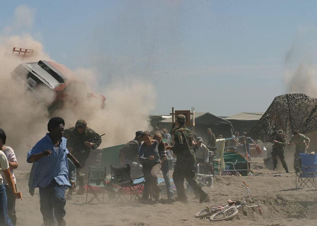 Civilians and soldiers run as a cloud of dust and cars rise behind them.