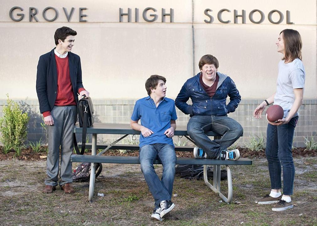 Four high school boys stand and sit around a picnic table laughing.