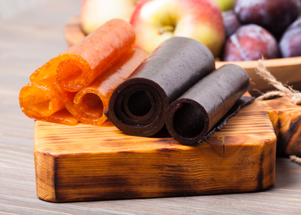 Rolls of orange and black fruit leather on a wooden board.