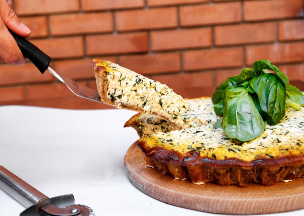 A hand cutting a piece of tofu quiche.