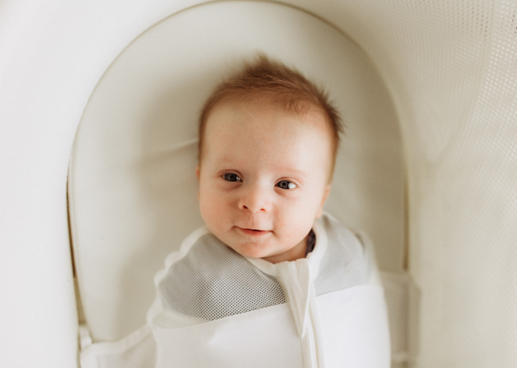 A baby zipped up in a sleep swaddle in a bassinet.