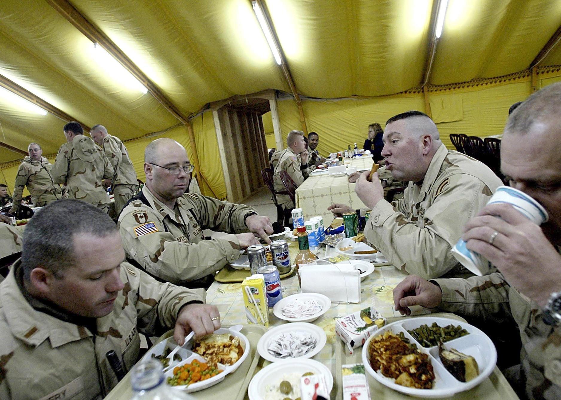 Soldiers eating in a large military tent.