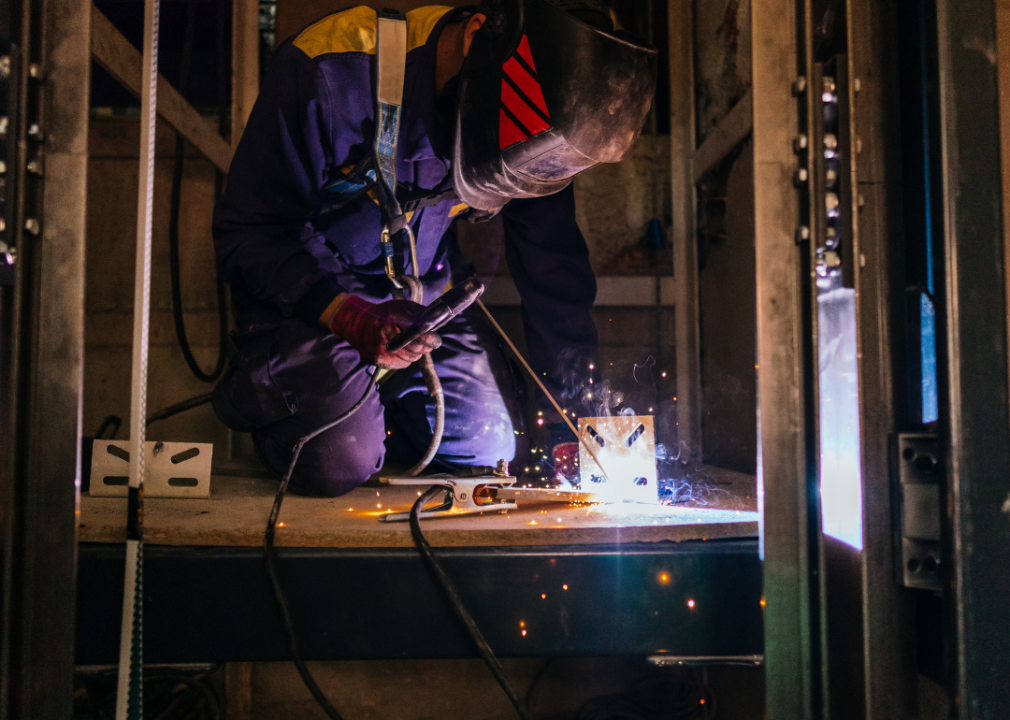 A person welding metal in an elevator under construction.