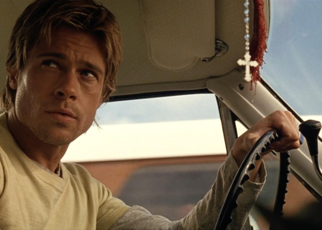 Brad Pitt driving an old truck with a cross hanging from the rearview mirror.