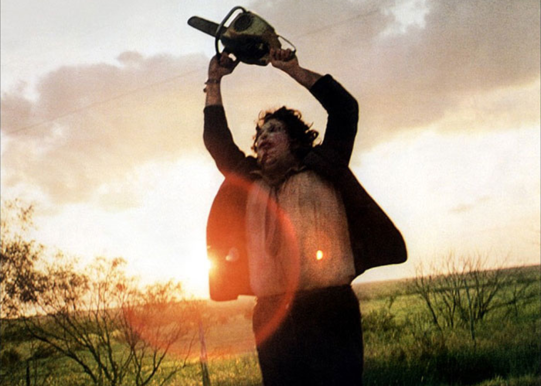 A man running with a mask on and waving a chainsaw in the air.