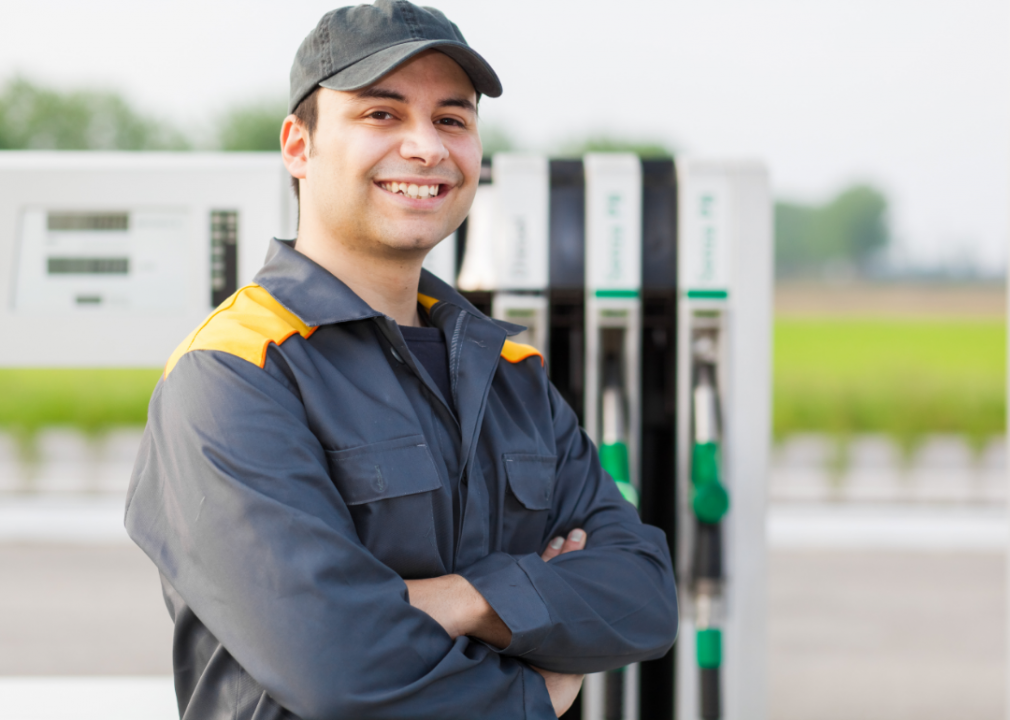A man smiles in front of gas pumps. 