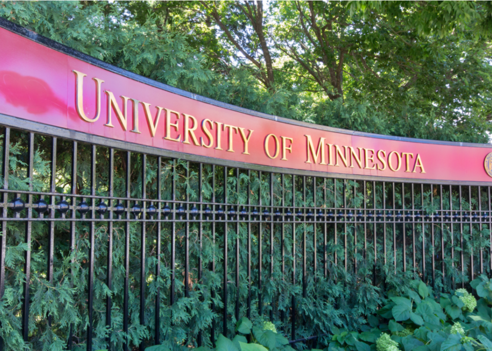 A red sign atop a wrought iron fence with gold letters spelling out University of Minnesota. 