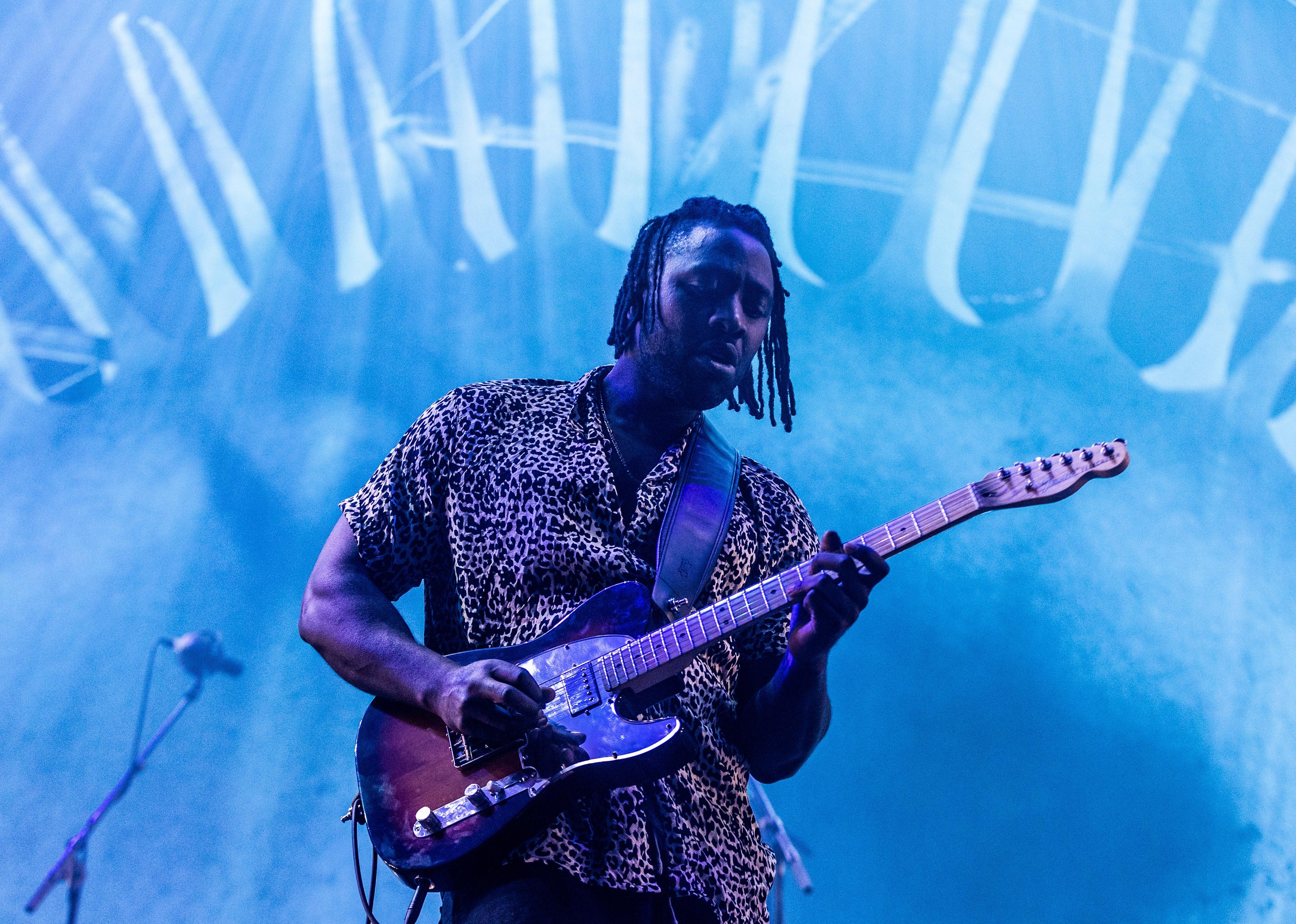 Kele playing guitar onstage in a leopard print shirt.
