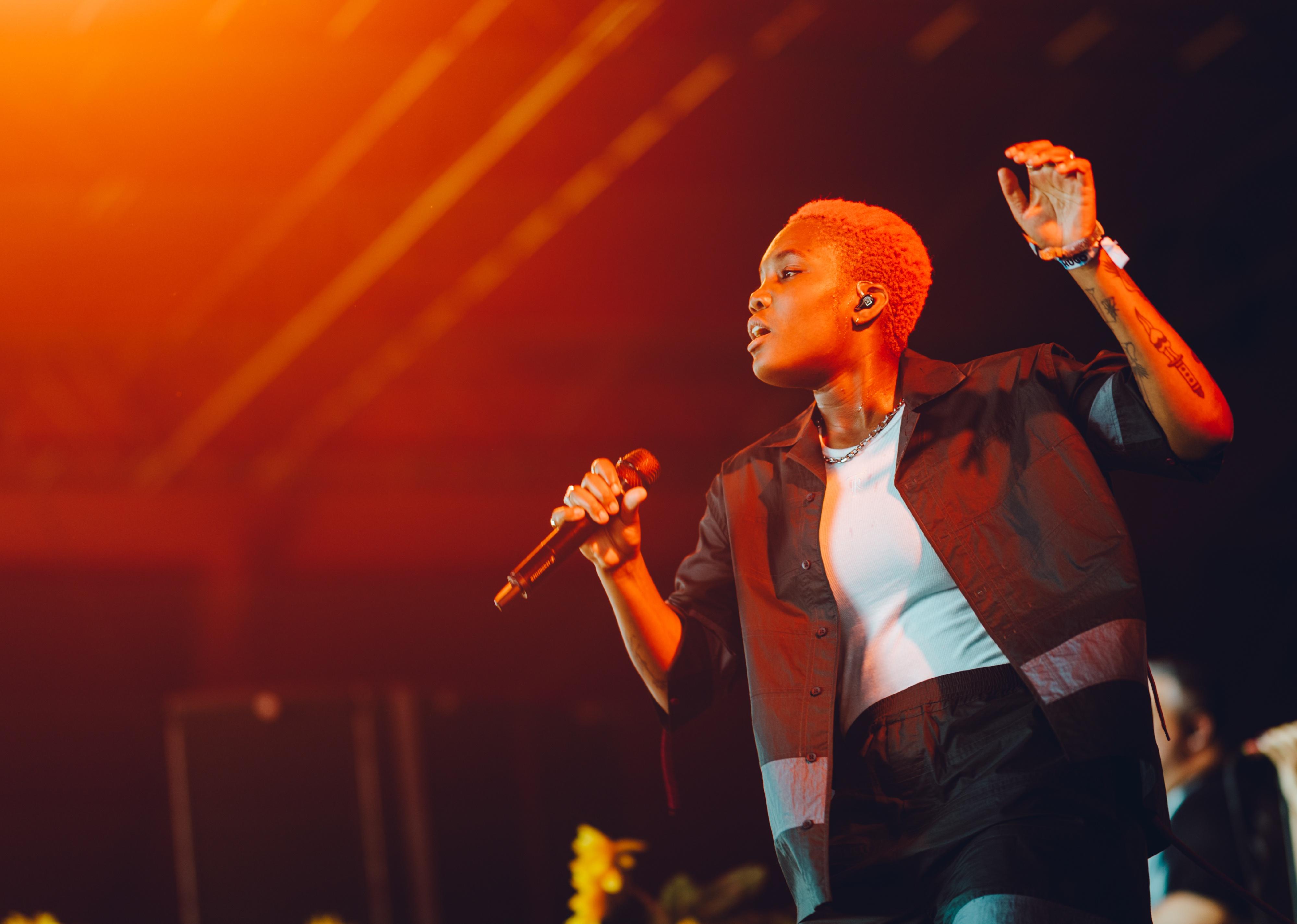 Arlo Parks performing onstage under orange light.