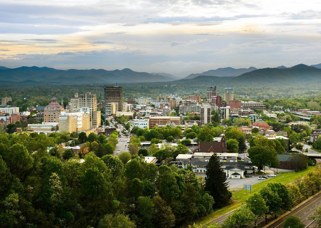 The skyline of downtown Asheville at sunset with mountains in the background.