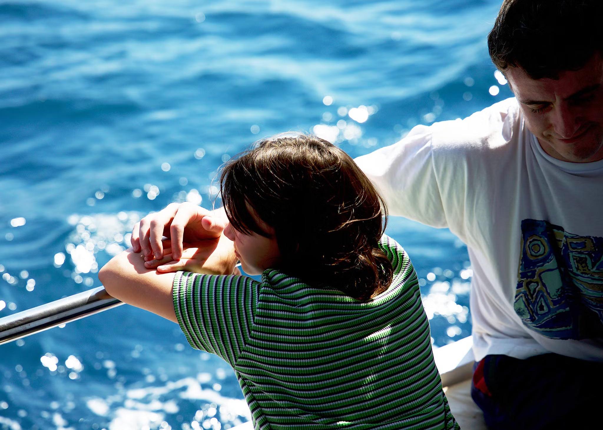 A father and daughter holding hands in the sun on a boat.