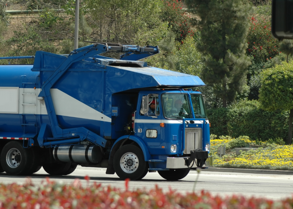 A blue waste management truck being driven down the road. 