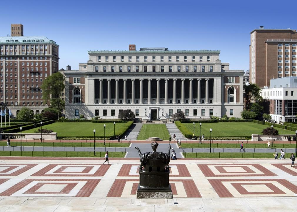 A view from behind the Alma Mater bronze sculpture, a person seated on a throne in an academic gown and wearing a laurel upon their head, on the steps of the Low Memorial Library on the campus of Columbia University.