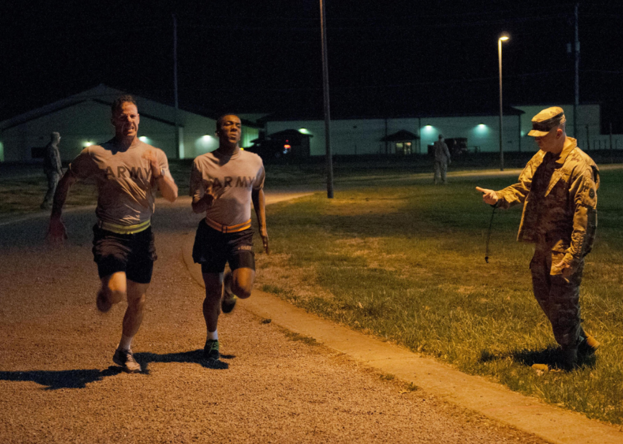 Guys in army shirts running on a track at night.