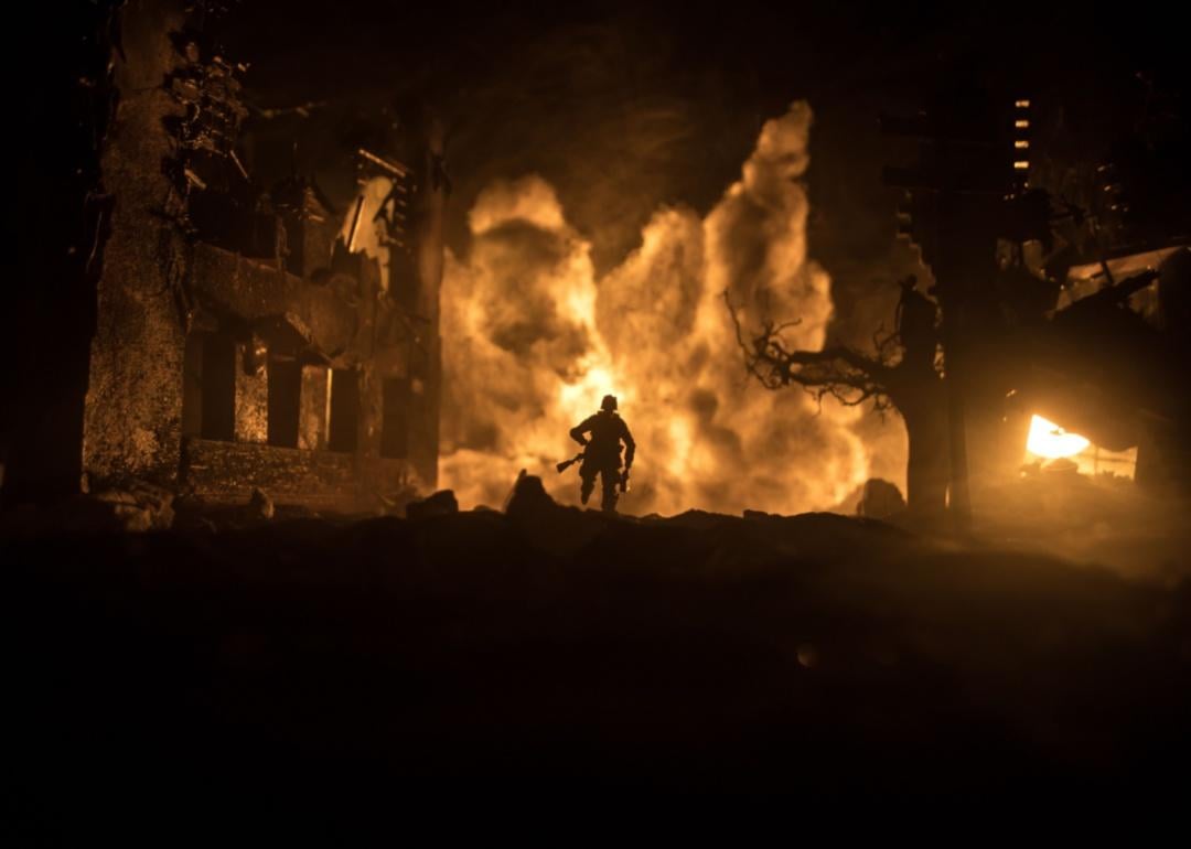 A soldier running from a burning building at night.